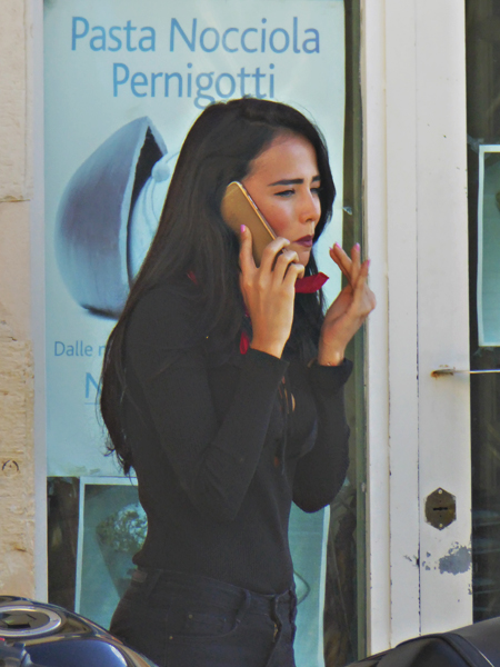 Very pretty girl, smacking her lips while on the phone and standing in front of pasta advertisment