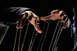 Image of two hands holding puppet strings against a black background