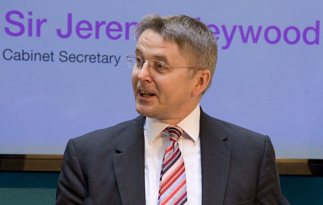 Lord Jeremy Heywood (deceased) in front of a banner saying that he was Cabinet Secretary